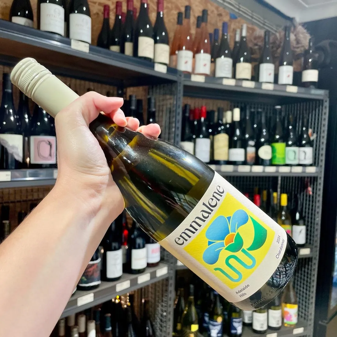 A hand holding a bottle of Emmalene Adelaide Hills Chardonnay in front of the wine shelves at Bottle Keg Can
